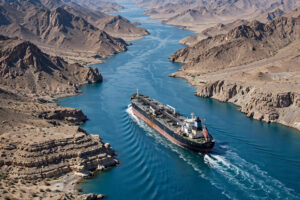 An oil tanker sailing through the Strait of Hormuz between arid mountainous coastlines