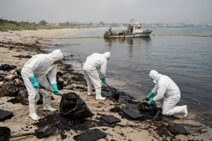 Workers in protective suits cleaning oil residue from a Gulf beach during the UAE coastal clean-up operation